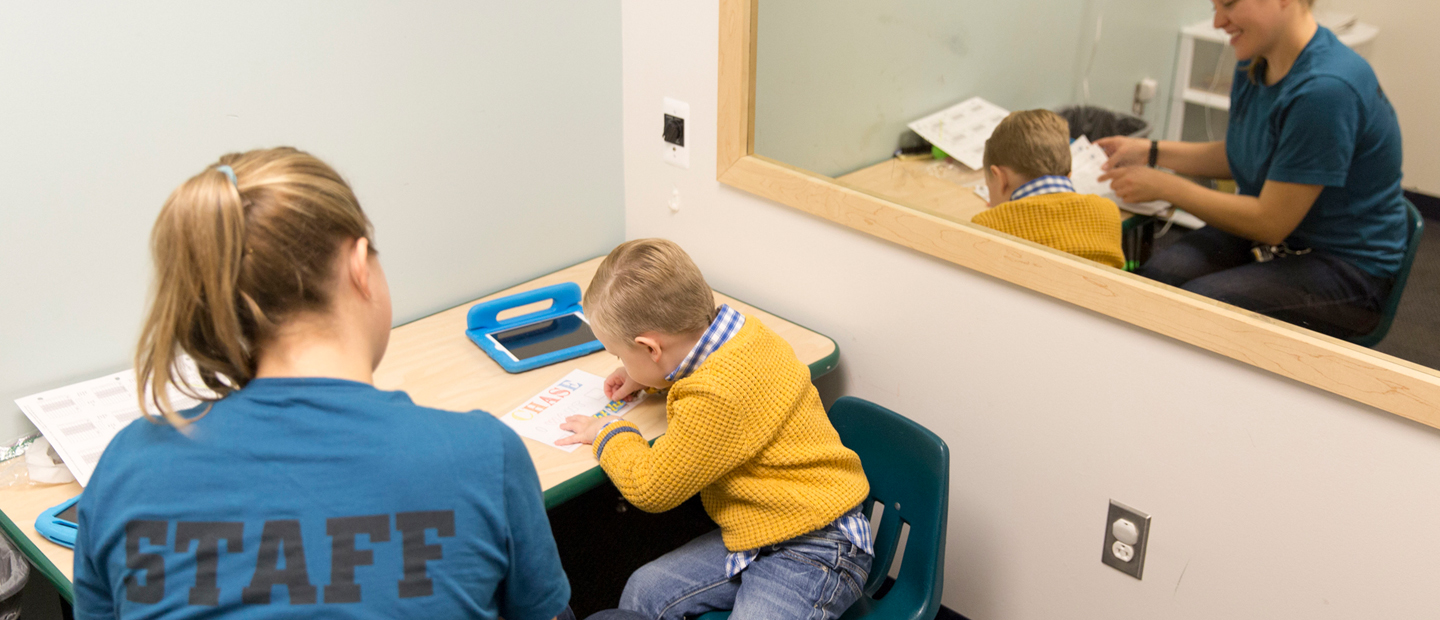 Woman and kid sitting at desk with kid writing something on paper