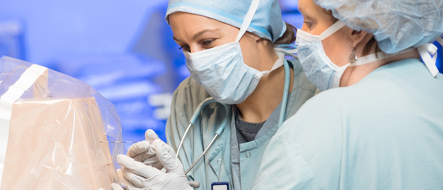 two women in surgical gowns and masks poking an object in a plastic cover